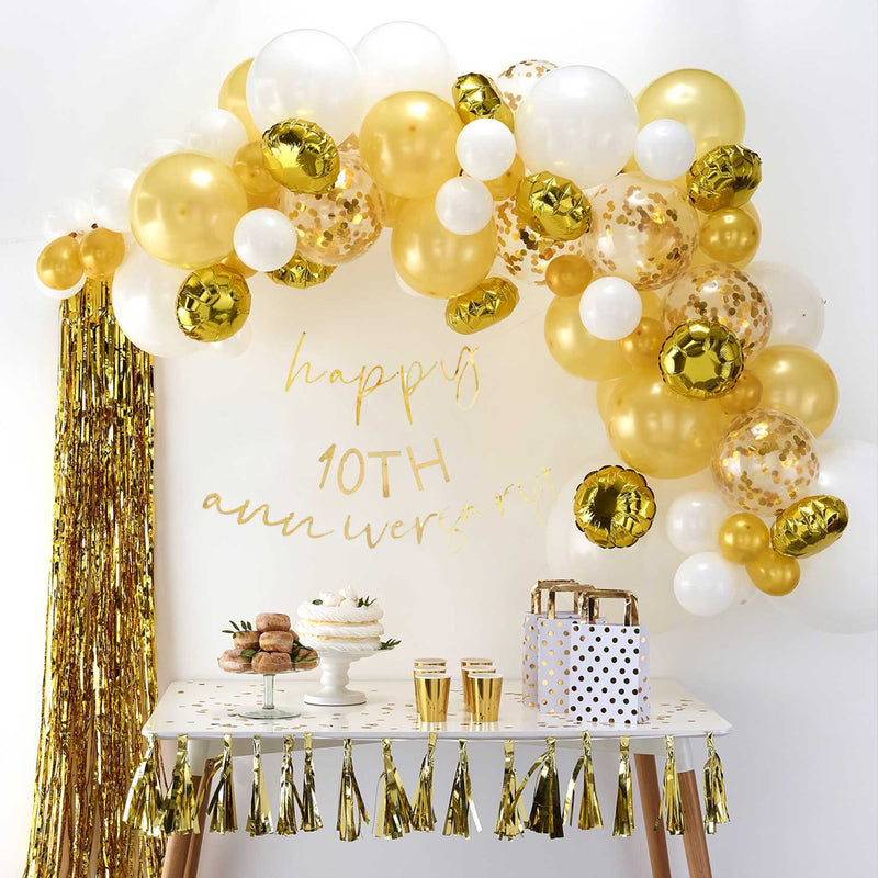 Tafel met hapjes drankjes en giftbags, onder een goud met witte boog van balonnen