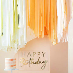 oranje perzikkleurige en goudkleurige crepe slingers met een taart en happy birthday bordje