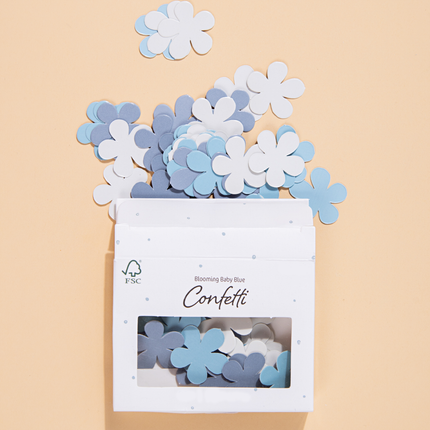 blauwe en witte confetti bloemen liggen op een gele ondergrond en zitten in een wit met blauw doosje