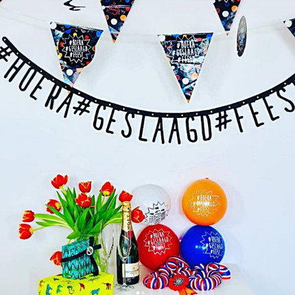zwarte slinger hoera geslaagd feest hangt boven rode tulpen en rood wit blauwe en oranje ballonnen