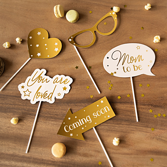 Photobooth props in het goud en nude voor een babyshower liggen op een houten tafel