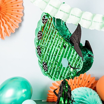 Pinata in de vorm van een dinosaurus hoofd hangt voor een blauwe muur en een oranje waaier