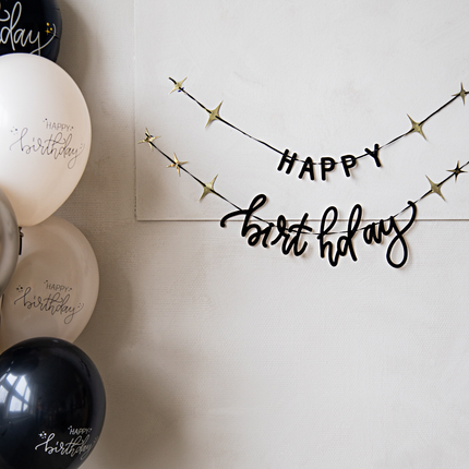 zwarte slinger met de tekst happy birthday en gouden sterren hangt aan een witte muur