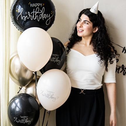 vrouw met een feesthoedje op en een bundel zwarte en creme ballonnen met de tekst happy birthday