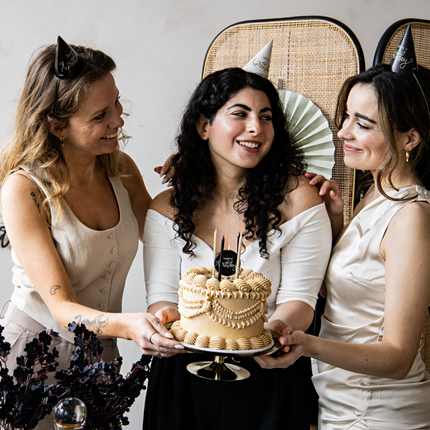 drie vrouwen houden een taart vast met beige, nude en zwarte versiering