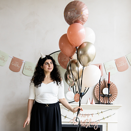 een vrouw met zwarte krullen houd een bos met roze en beige ballonnen vast