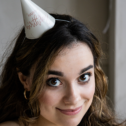 vrouw met een wit feesthoedje met de roze tekst happy birthday