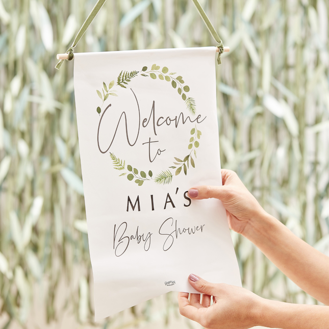 Wit uithangbord hangt voor groen blad met de tekst 'Welcome to Mia's babyshower'