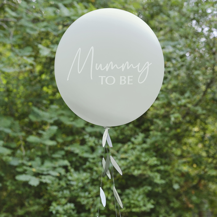 Sagegroene ballon met ballonstaart met bladeren eraan en de witte tekst mummy to be hangt voor groene bosjes