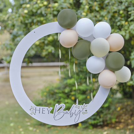 Wit fotoframe met de tekst hey baby en groene, nude en witte ballonnen hangt in een groen grasveld
