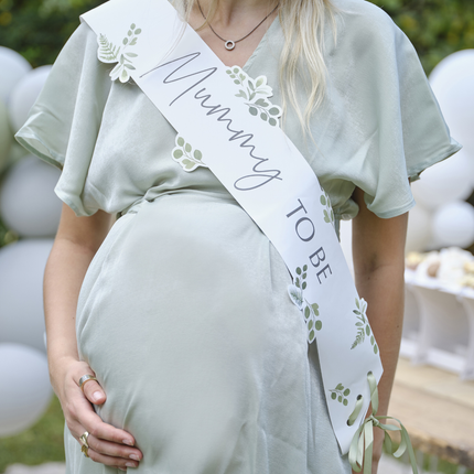 Zwangere vrouw in lichtgroene jurk draagt een sagegroene sjepr met bladeren en de tekst mummy to be