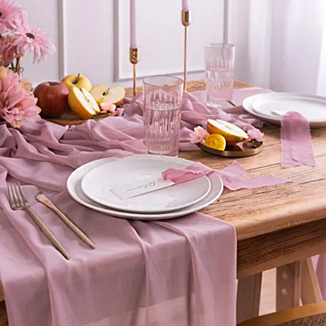 chiffon tafelloper in de kleur lila ligtop een houten tafel omrings met lila lint en kunstbloemen