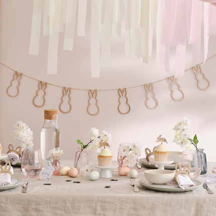 Gedekte tafel met paaseieren, witte konijntjes, cupcakes en een houten slinger