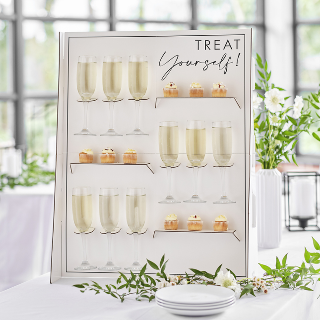 Hapjes en drankjes standaard met champagneglazen en cupckes staat op een witte tafel versierd met witte bloemen en groene takken