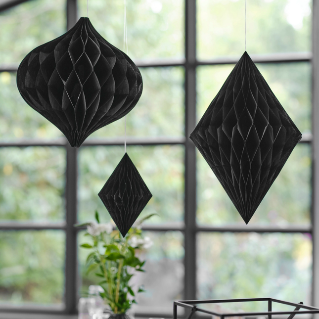 Drie zwarte honeycombs hangen voor een raam met zwarte kozijnen