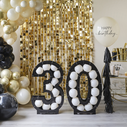 Gouden backdrop hangt aan een witte muur en ervoor staat een ballonstandaard nummer 30 gevulde met witte ballonnen