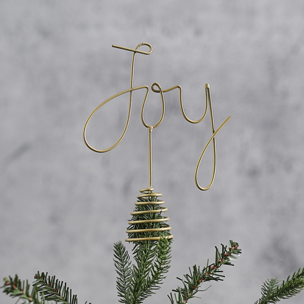 Gouden piek met de tekst joy zit bovenop een groene tak voor een grijze muur