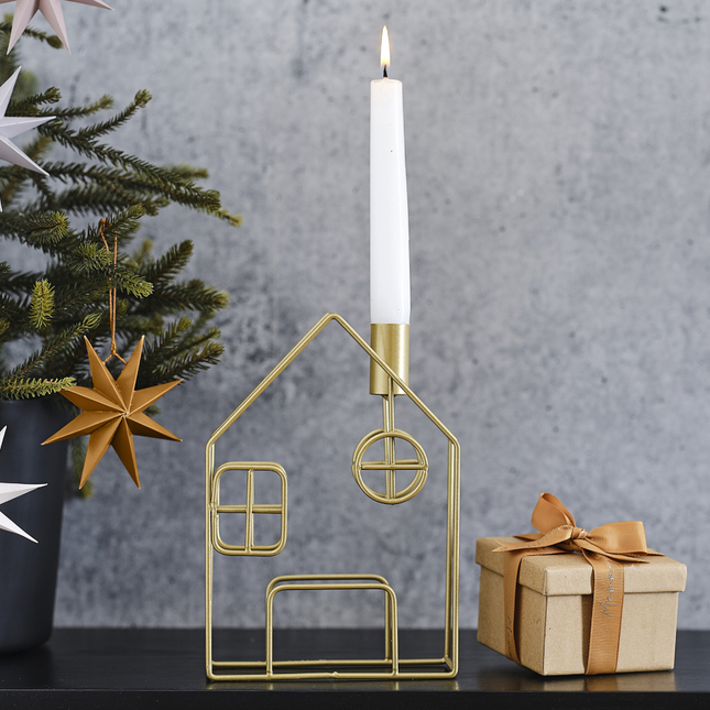 Gouden kaarshouder in de vorm van een huisje staat op een zwarte tafel naast een groen boompje en een kartonnen cadeautje met koperen strik
