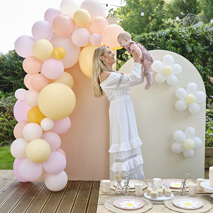Moeder houd haar baby vast en staat naast een ballonnenboog en madeliefjes versiering
