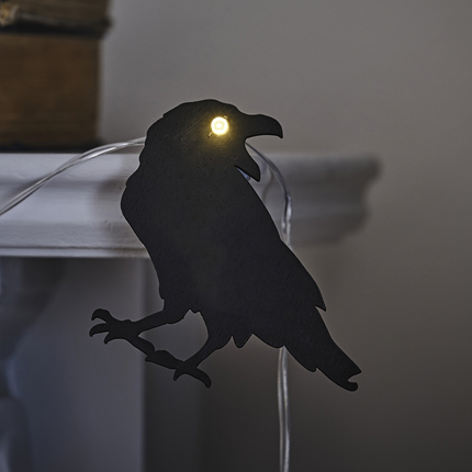 Houten, zwarte kraai met lichtgevens oog hangt voor een witte schoiuw