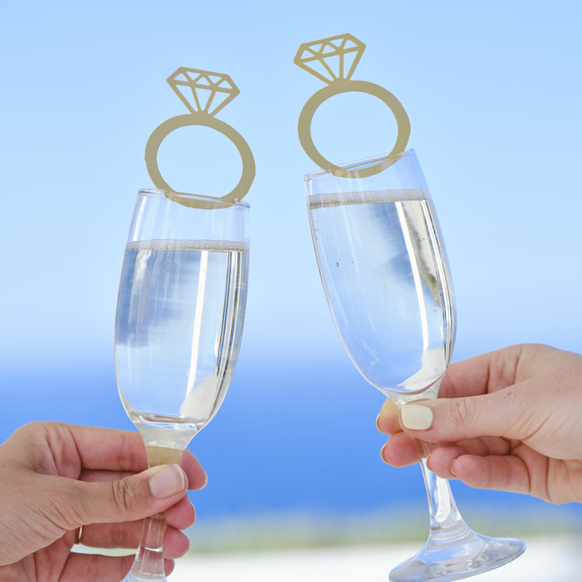 Champagneglazen worden vastgehouden voor een blauwe zee en zijn versierd met een gouden drankjestopper in de vorm van een ring