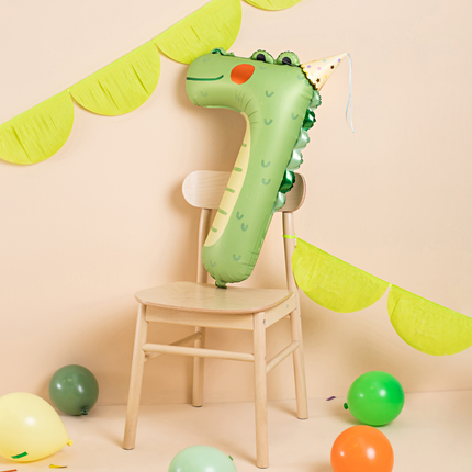 folieballon krokodil cijfer 7 zit op een zit met een feesthoedje op naast groene slingers en ballonnen
