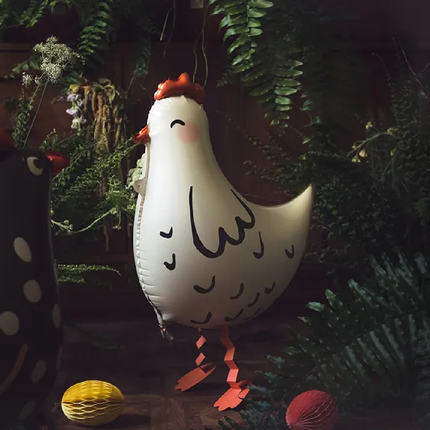 Witte folieballon in de vorm van een kip staat in een zwarte ruimte met palmbladeren