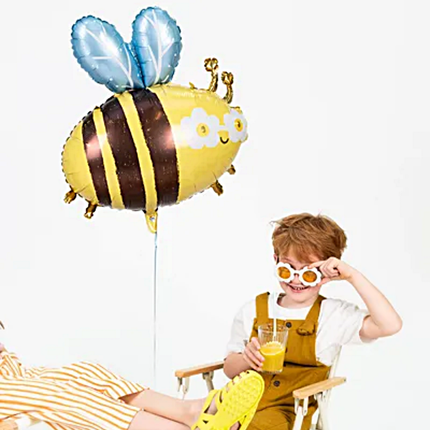 Cool kind met madeliefjes zonnebril houd een hommel ballon vast en zit op een gele tuinstoel
