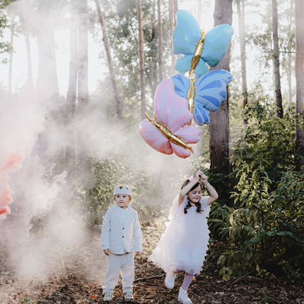 twee kinderen spelen in een bos met drie vlinder ballonnen in het blauw, mint en roze