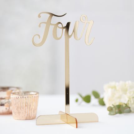 Gouden tafelnummer op standaard staat op een witte ondergrond met witte rozen