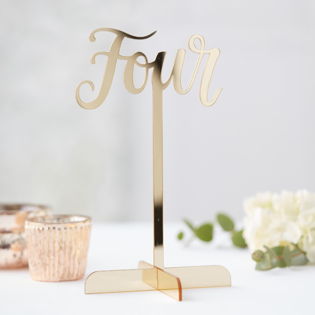 Gouden tafelnummer op standaard staat op een witte ondergrond met witte rozen