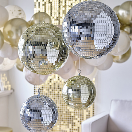 Zilveren en gouden discoballen hangen in een ruimte versierd met een gouden backdrop