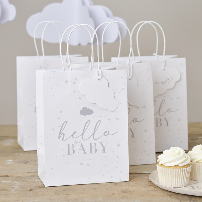 Witte giftbags voor een babyshower staan op een houten tafel naast cupcakes en erboven hangen witte wolkjes