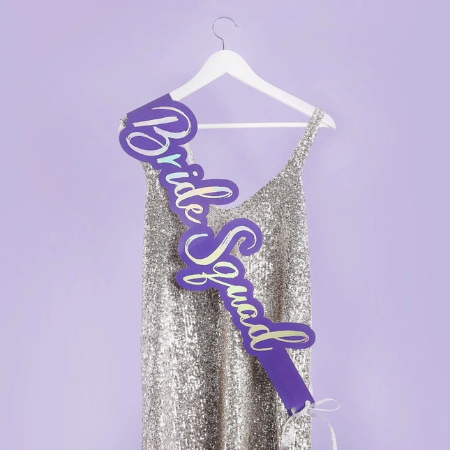 Paarse sjerp hangt over een zilveren glitter jurk aan een witte hangen voor een lila achtergrond