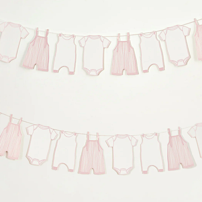 Slinger met roze en witte rompertjes hangt voor een lichtgrijze muur