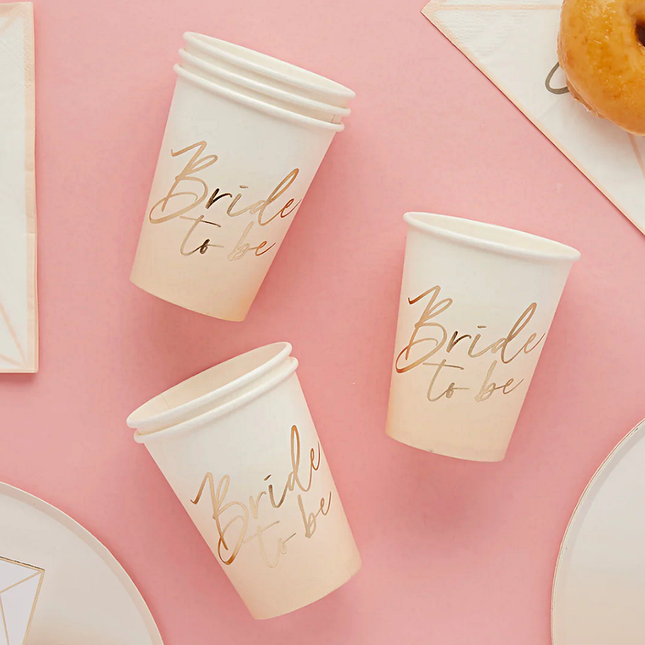 perzik en witte ombre bekers met de gouden tekst bride to be liggen op een roze tafel