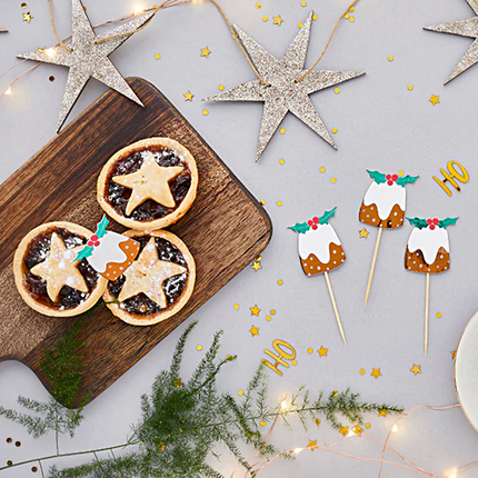 Houten dienblad gevuld met gebakjes met prikkers en houten kerststerren liggen op een witte tafel