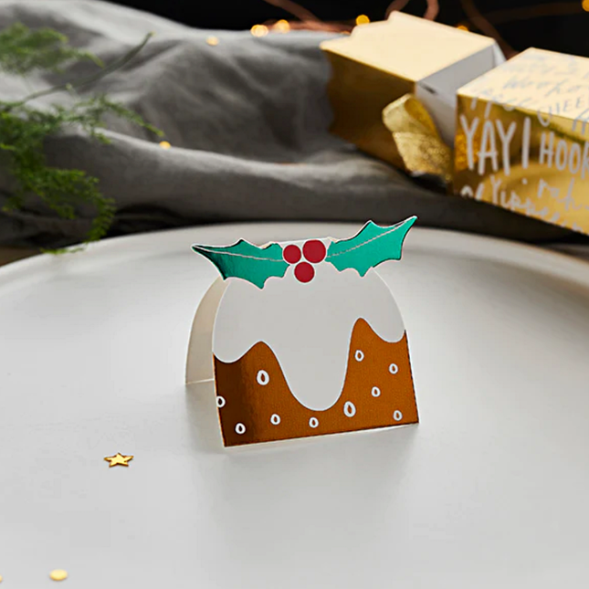 Tafelkaartje in de vorm van een pudding staat op een wit bord naast een groene tak