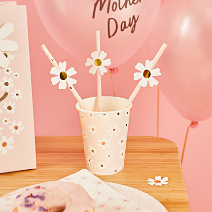 Roze beker met madeliefjes staat op een houten tafel en is gevuld met bijpassende rietjes