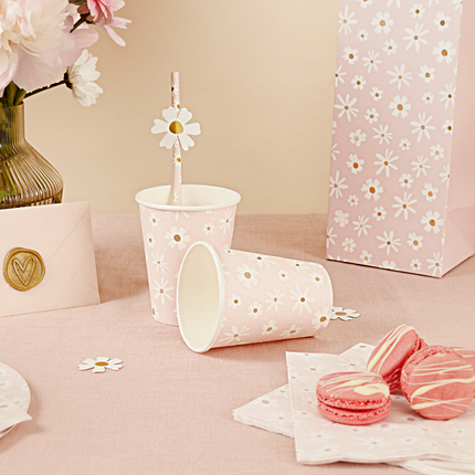 Roze beker met madeliefjes staat op een roze kleed naast roze macarons