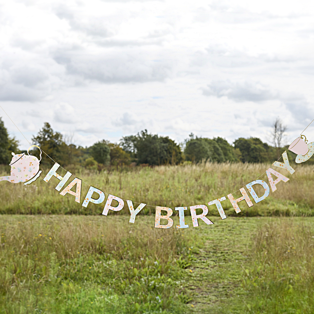letterbanner happy birthday pastel bloemen en theekopjes hangt in een grasveld