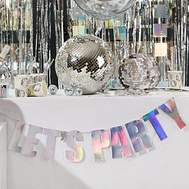 iridescent letterbanner met de tekst lets party hangt aan een versierde tafel met discoballen