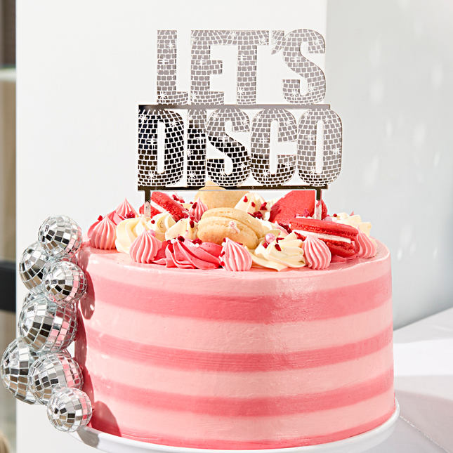 zilveren taart topper met de tekst lets disco zit bovenop een roze taart met fruit en discoballen