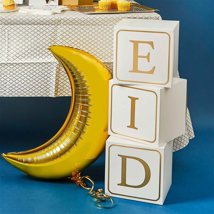 Witte blokken met gouden letters EID staan op een blauwe ondergrond naast een gouden ballon in de vorm van een halve maan