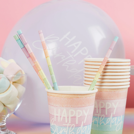 Rietjes met regenboogpatroon in pasteltinten zitten in een pastelkleurige beker voor een paarse ballon