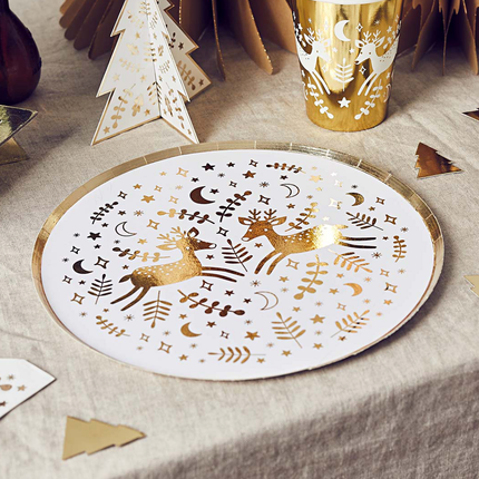 Wit bordje met gouden print en gouden rand ligt op een katoenen, beige tafellaken naast gouden confetti in de vorm van kerstbomen
