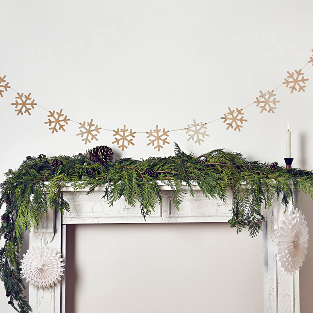 Slinger met houten sneeuwvlokken hangt boven een witte schouw versierd met bladgroen