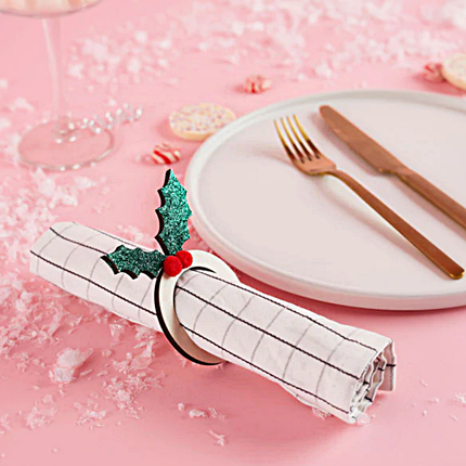 Houten servettenringen met een groene glitterhulst en rode pompoms ligt op een roze tafel met nepsneeuw