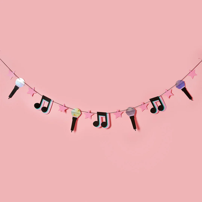 slinger met muzieknootjes, microfoontjes en roze sterren hangt voor een roze muur