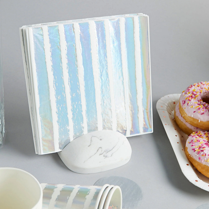 witte en iridescent gestreepte servet zit in een witte servet houder naast een schaal roze donuts